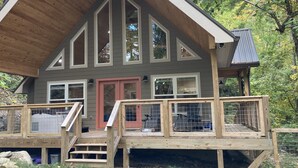 Una cabaña con terraza de madera, varias ventanas y una puerta roja.