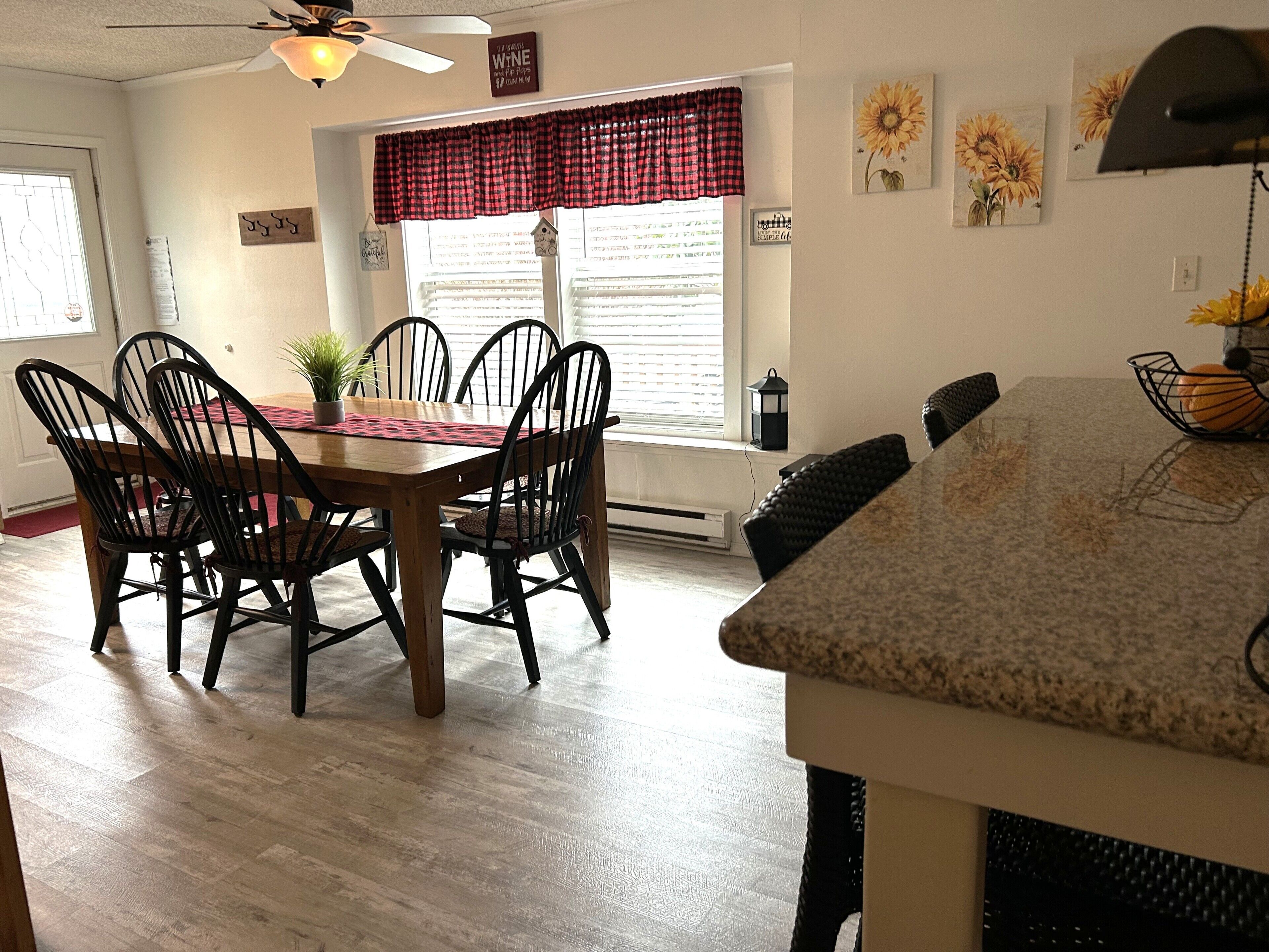 Un coin repas avec une table et des chaises en bois, une fenêtre avec des stores et un ventilateur de plafond.