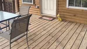 Une cabane en bois avec un porche, une table à manger avec des chaises et une statue de chien jaune.