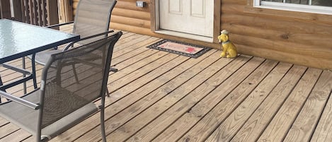 A wooden cabin with a porch, a dining table with chairs, and a yellow dog statue.