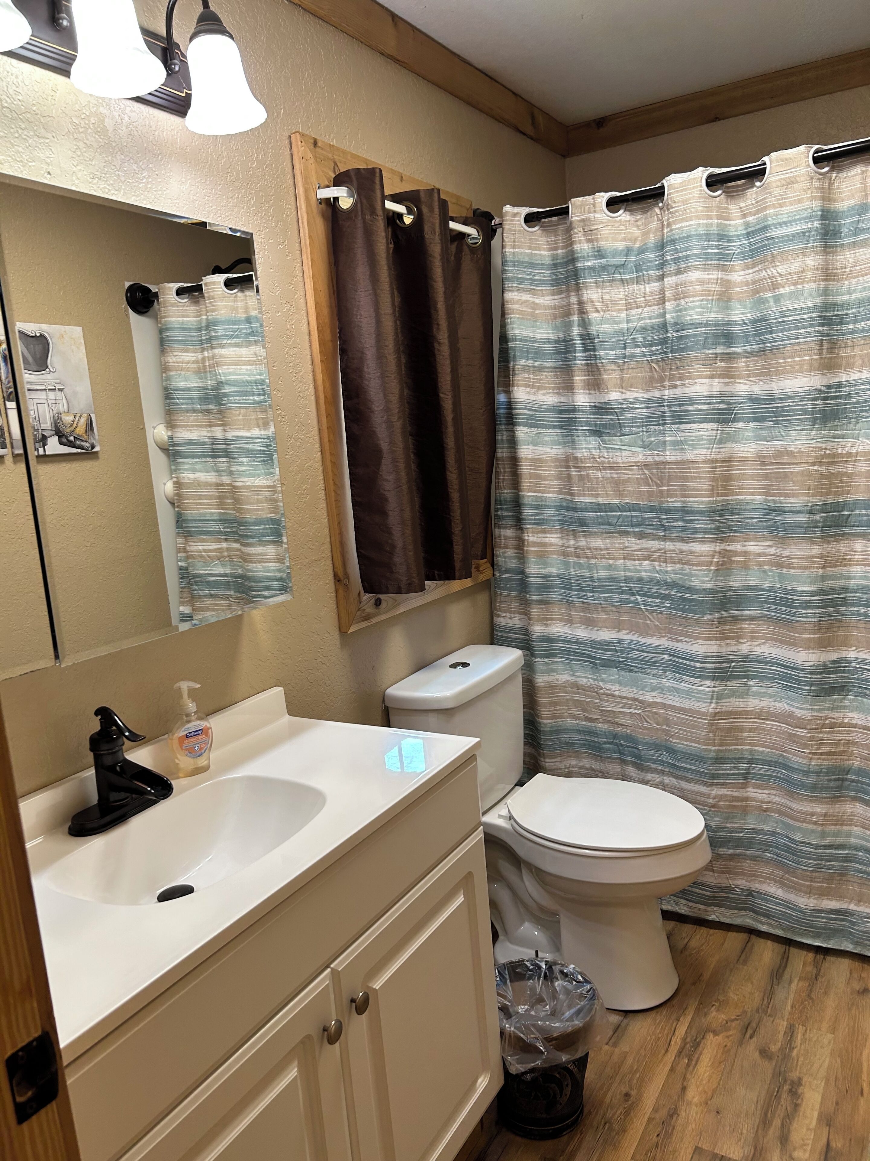Une salle de bain avec un lavabo blanc, un robinet noir et un miroir au-dessus. On y trouve des toilettes avec un abattant blanc et un rideau de douche à rayures.