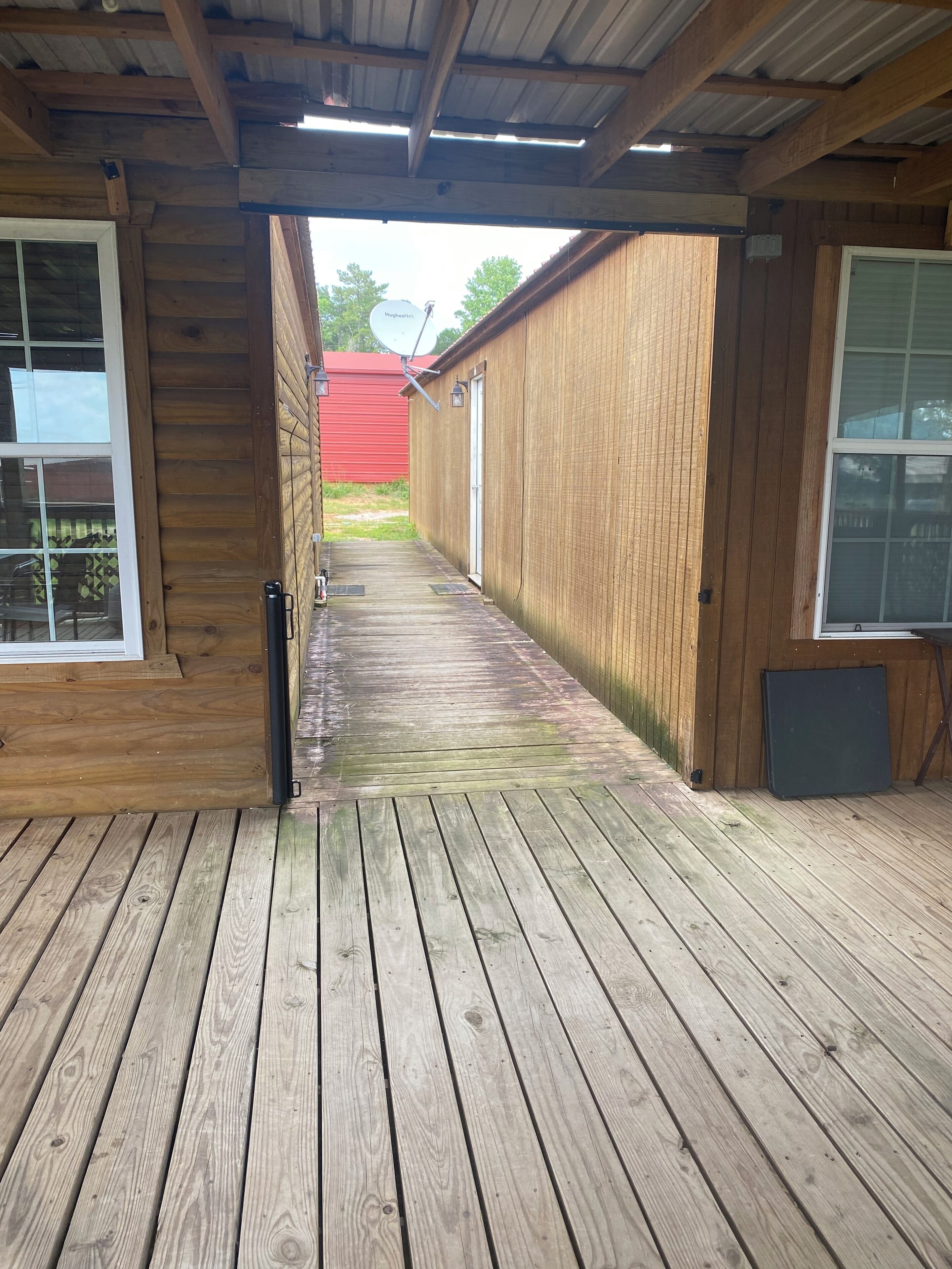 A wooden deck leading to a building with a red exterior and a satellite dish.