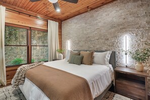 A bedroom with a wooden ceiling, a brick wall, a large bed with a brown blanket, and two bedside tables with plants. - HUGE Game Rm w/Pool Table, A+ Location, Hot Tub (Gatlinburg)