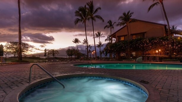 A pool area with a circular hot tub, palm trees, and a building with a balcony. - Affordable quality in central location, Oceanside Complex  (Kihei)