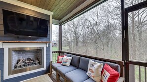 Ein gemütlicher Außenbereich mit Kamin, Fernseher und Blick auf Bäume.
