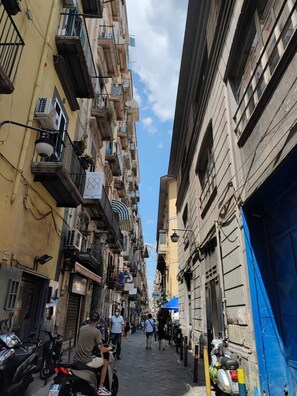 A narrow street flanked by multi-story buildings with balconies, a few parked scooters, and pedestrians. - B&B L'Infinito 88 Charmant Rooms - Room 1 - King Superior with balcony (Napoli)