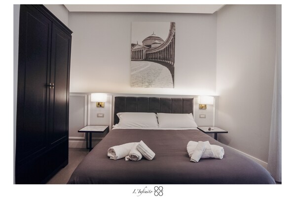 A hotel room with a large bed, two bedside tables, a dark wardrobe, and a framed picture on the wall. - B&B L'Infinito 88 Charmant Rooms - Room 1 - King Superior with balcony (Napoli)