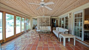 Um pátio espaçoso com um ventilador de teto, uma mesa de centro de vidro e um sofá branco.