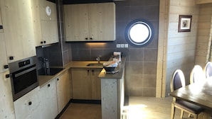 A modern kitchen with wooden cabinets, a built-in oven, and a round window above the sink. - Gorgeous appartment in Avoriaz (Avoriaz)