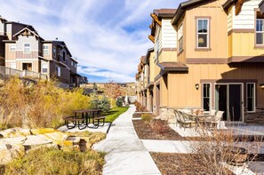 Zona residencial con un sendero que lleva a una hilera de casas adosadas, mobiliario de exterior y un pequeño jardín.