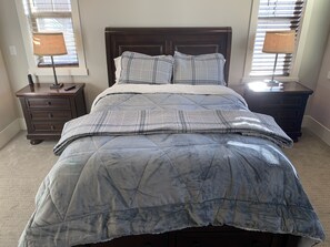 Una cama con una colcha acolchada, dos almohadas y un cabecero de madera. Hay dos mesitas de noche con lámparas y un pequeño aparador.