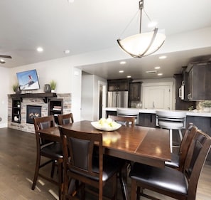 A modern kitchen with dark cabinetry, a central island, and a dining area with a wooden table and chairs.