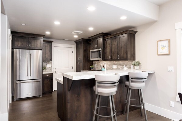 A modern kitchen with dark wood cabinets, stainless steel appliances, and a central island with bar stools.