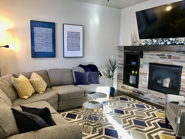 Una sala de estar con un sofá modular, una chimenea y dos obras de arte enmarcadas en la pared.