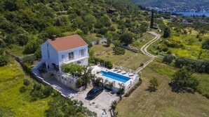 Ein zweistöckiges Haus mit Swimmingpool, umgeben von viel Grün und einer hügeligen Landschaft.
