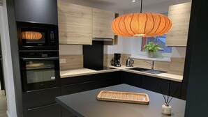 A modern kitchen with a built-in oven, a coffee maker, and a wooden island with a tray. - "LE SESAME" charming gite near Colmar (Wickerschwihr)