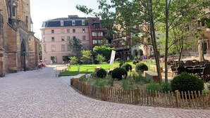A cobblestone street with historic buildings, a green park area, and outdoor seating. - "LE SESAME" charming gite near Colmar (Wickerschwihr)