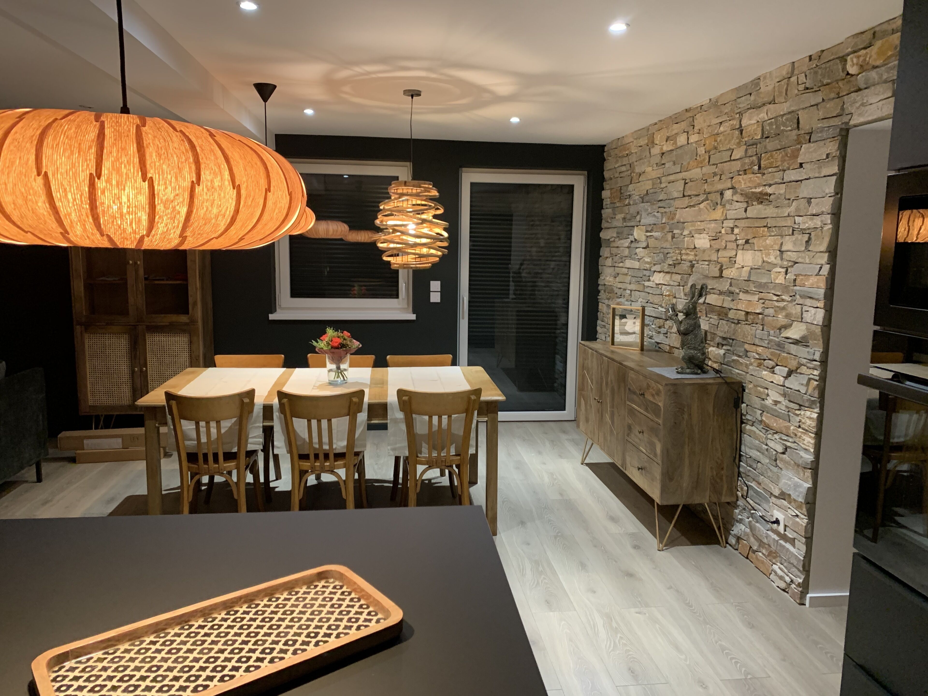 Une cuisine moderne avec un mur de crédence en pierre, des armoires en bois et un coin repas comprenant une table et des chaises.