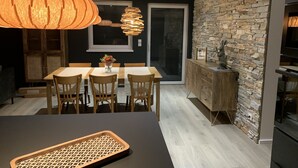 A modern kitchen with a stone wall backsplash, wooden cabinets, and a dining area with a table and chairs. - "LE SESAME" charming gite near Colmar (Wickerschwihr)