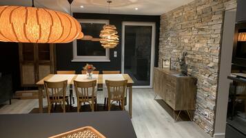 Une cuisine moderne avec un mur de crédence en pierre, des armoires en bois et un coin repas comprenant une table et des chaises.