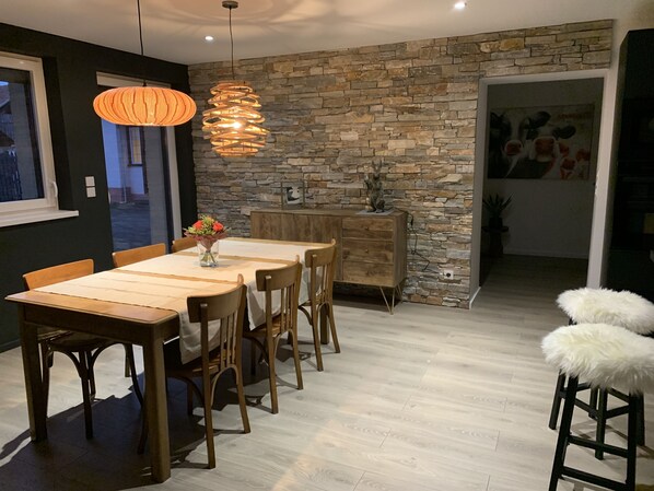 Comedor con mesa de madera, sillas y pared de piedra de fondo.