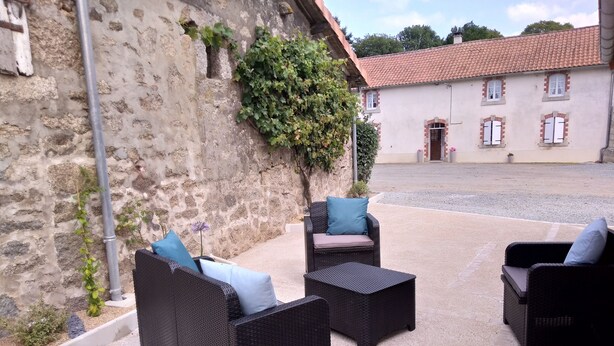 Ulkoterassi, jossa on rottinkihuonekaluja ja -tyynyjä, kiviseinä sekä taustalla näkyvä rakennus, jonka katto on päällystetty tiilillä.