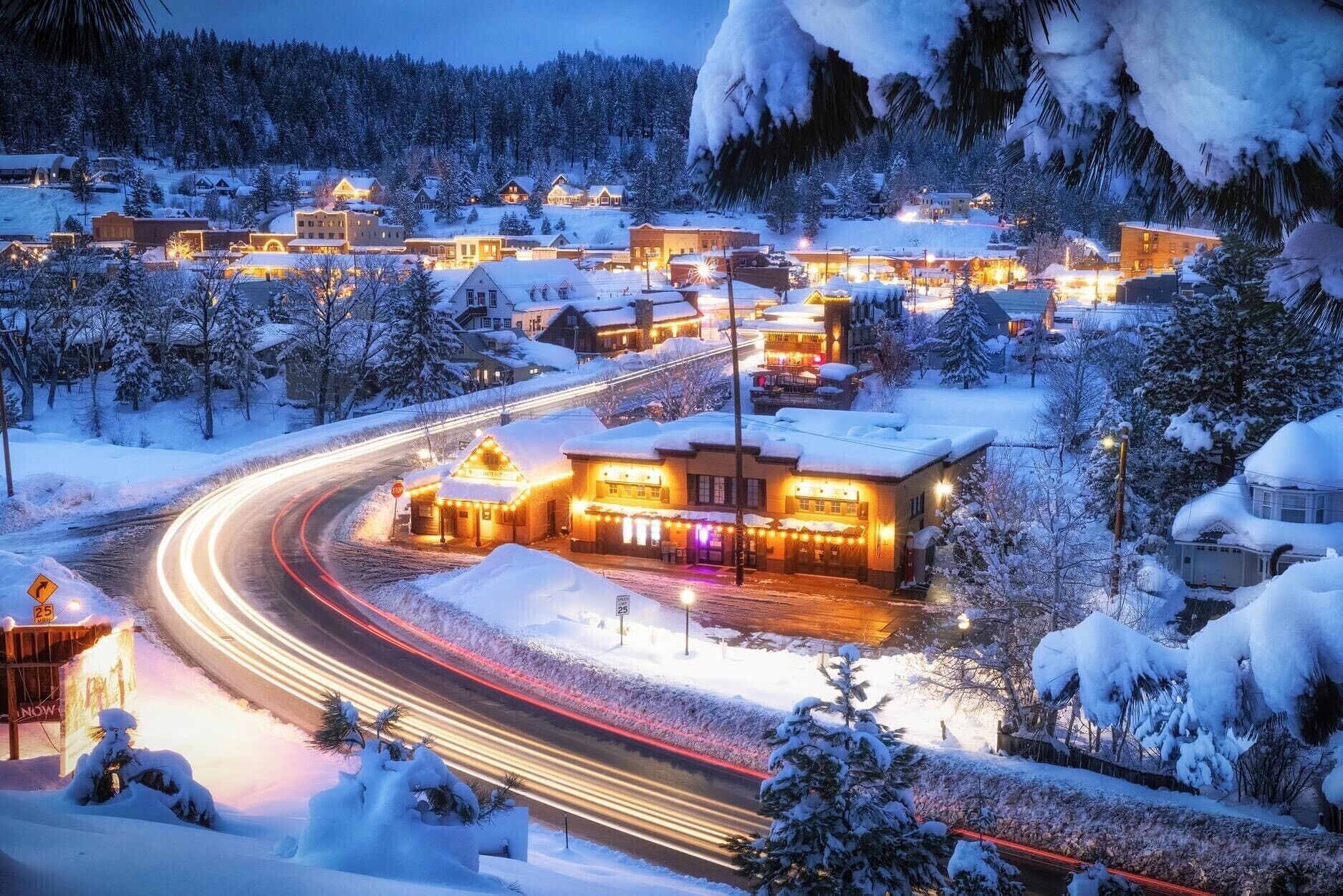 Une ville recouverte de neige, avec des bâtiments illuminés et une route sinueuse.