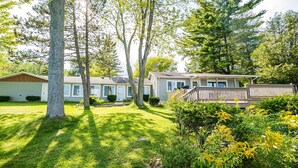 A single-story house with a front porch, surrounded by a well-maintained lawn and various trees. - Lexington Beach house, On the water with private beach (Lexington)