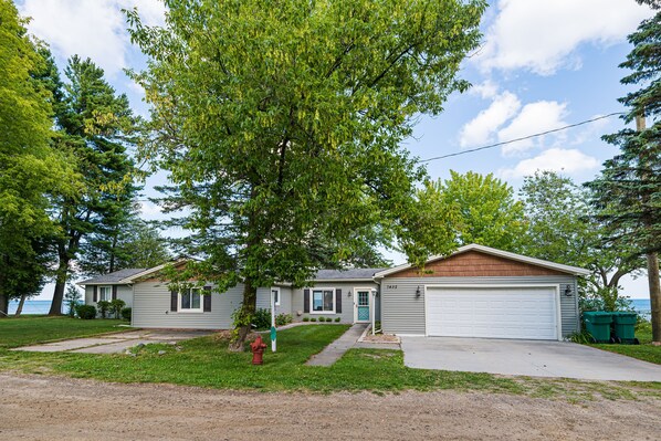 A two-story house with a garage, a front yard with a tree, and a view of the water. - Lexington Beach house, On the water with private beach (Lexington)