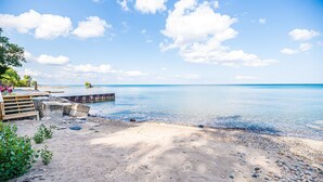 A beach with a wooden deck, clear blue water, and a sandy shore. - Lexington Beach house, On the water with private beach (Lexington)