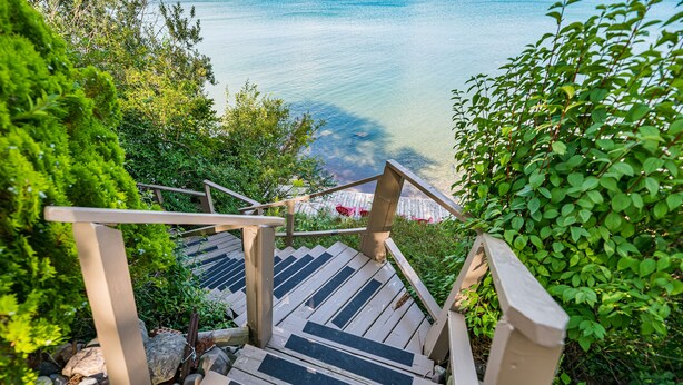 A wooden staircase leading to a beach with clear water, surrounded by greenery. - Lexington Beach house, On the water with private beach (Lexington)