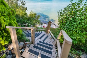 A wooden staircase leading to a beach with clear water, surrounded by greenery. - Lexington Beach house, On the water with private beach (Lexington)