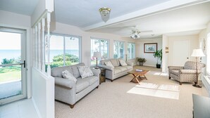 A spacious living room with a large window overlooking a scenic view, a ceiling fan, and a cozy seating area with a coffee table. - Lexington Beach house, On the water with private beach (Lexington)