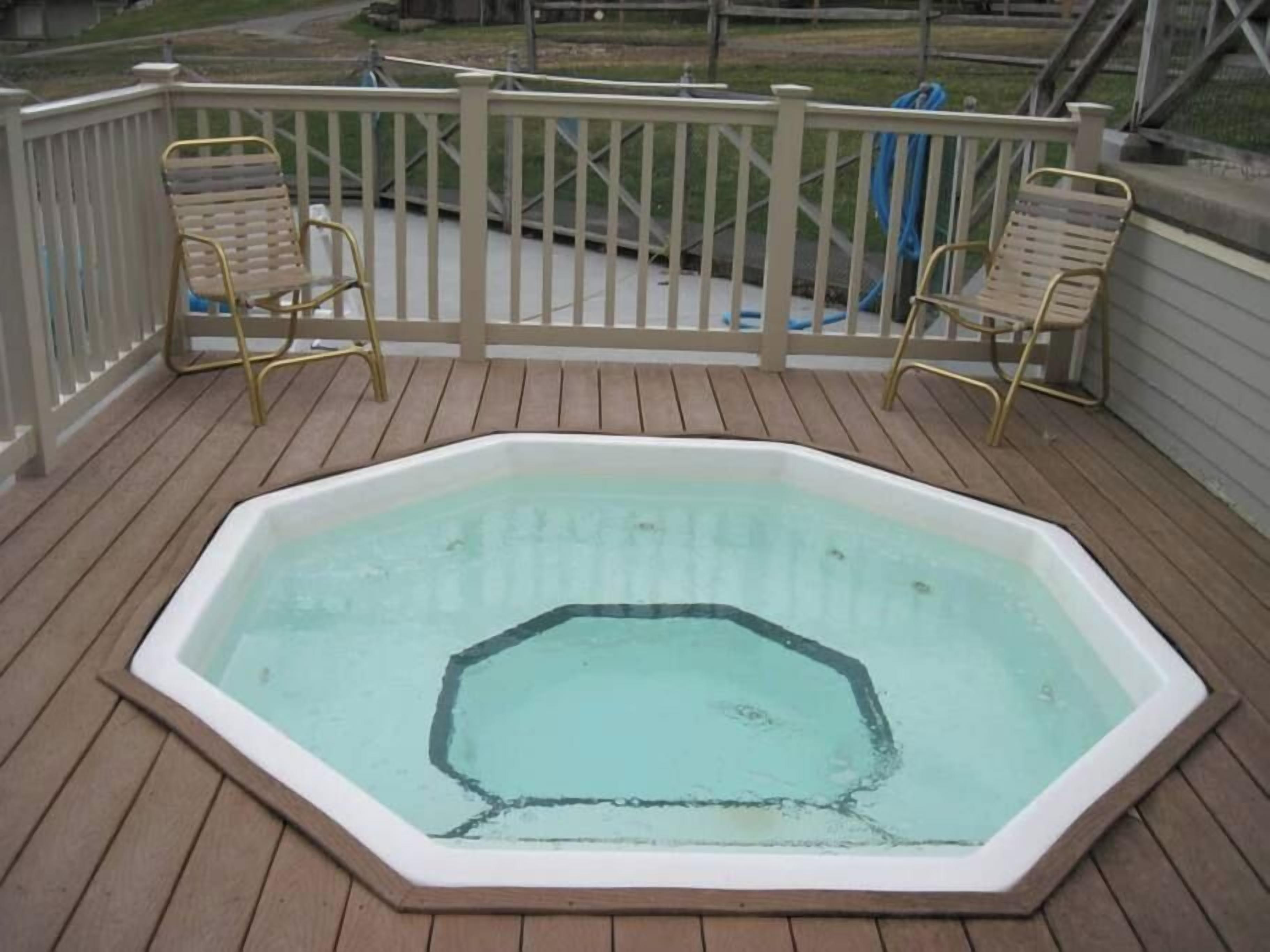Un jacuzzi en una terraza de madera con barandilla blanca y dos sillas.