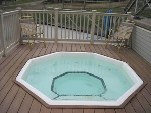 Un bain à remous sur une terrasse en bois, avec une balustrade blanche et deux chaises.