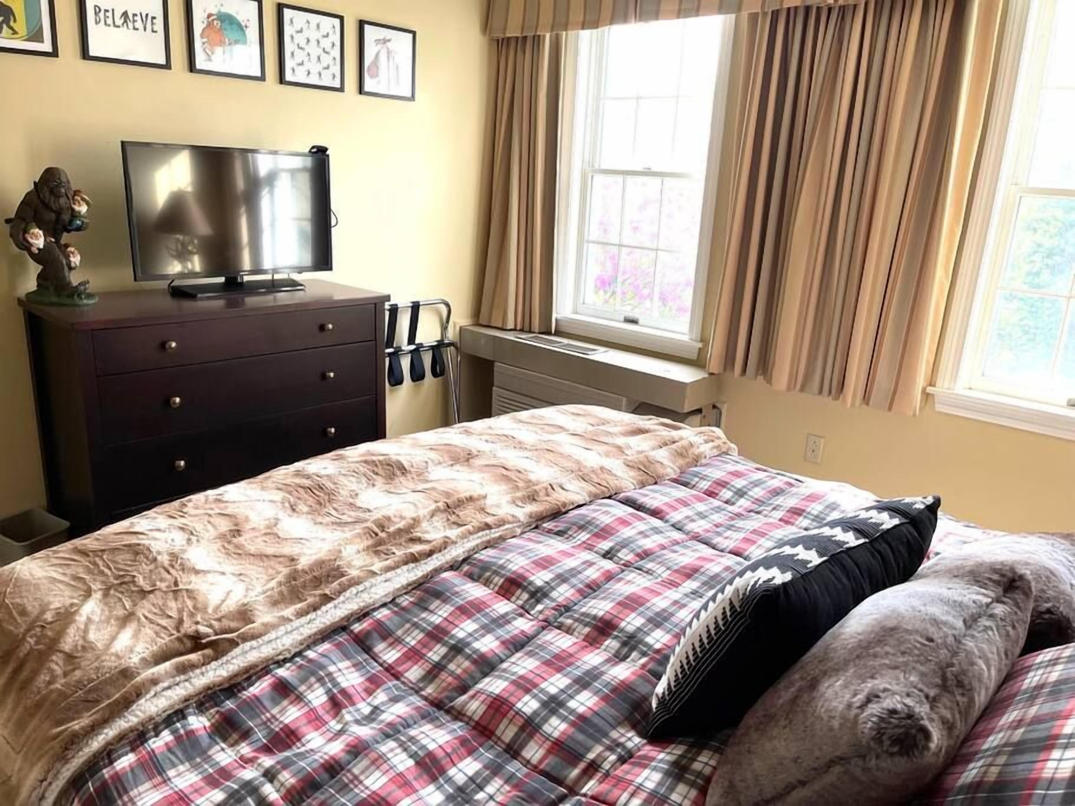 Un dormitorio con cama, cómoda, televisor y ventana con cortinas.