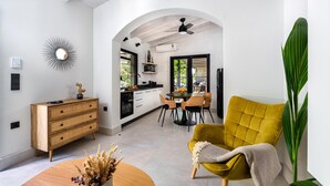 A modern kitchen with white cabinets, a dining area with a yellow chair, and a large plant. - Two Bedroom Villa with Private pool just 100m from the Beach (Heraklion)