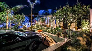 A modern house with a garden, a black sports car, and a well-lit patio area. - Two Bedroom Villa with Private pool just 100m from the Beach (Heraklion)