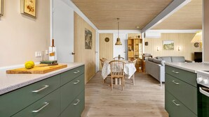 Eine moderne Küche mit grünen Schränken, einem Holzespeisetisch und einer gemütlichen Wohnbereits mit Sofa und Fernseher.