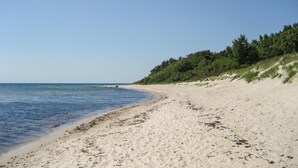 Ein Sandstrand mit sanften Wellen, einem klaren Himmel und einem bewaldeten Hügel.
