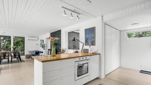 Een moderne keuken met witte kastjes, een houten aanrechtblad en een oven. Op het aanrecht staat een vaas met bloemen, en aan de muur hangt een ingelijst beeld.