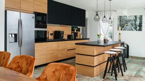 Een moderne keuken met houten kastjes, een roestvrijstalen koelkast, een koffiezetapparaat en een bar met krukjes.