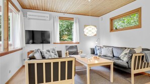 Ett modernt vardagsrum med ett träpanelat tak, en platt-TV, en soffa, ett soffbord och ett matbord.