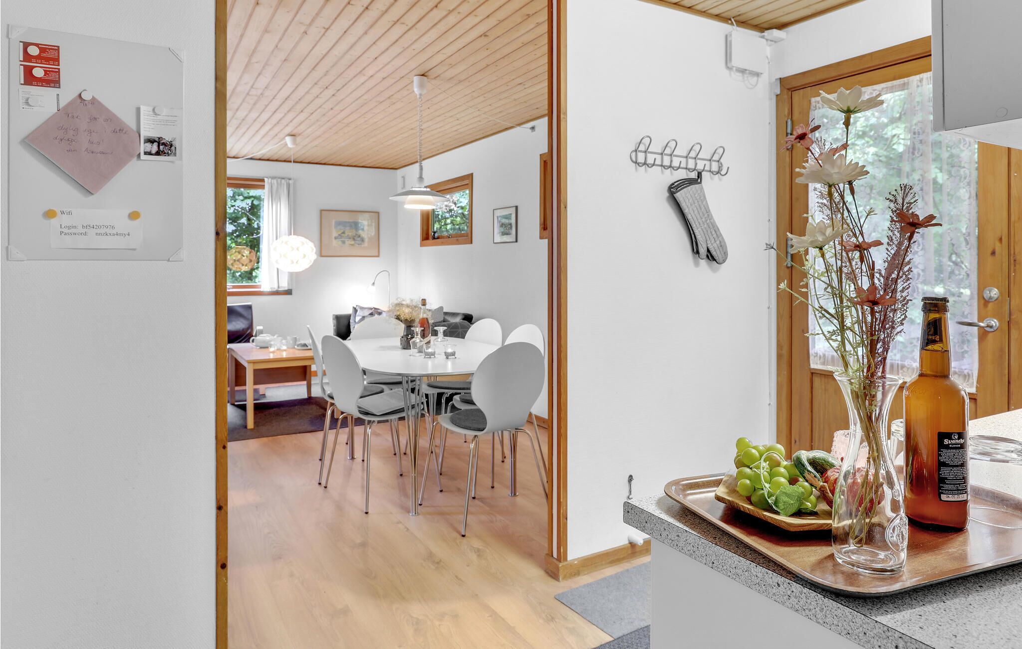 Een moderne keuken met een houten plafond, een eethoek met een ronde tafel en stoelen, en een aanrecht met een fles en een bloemenvaas.