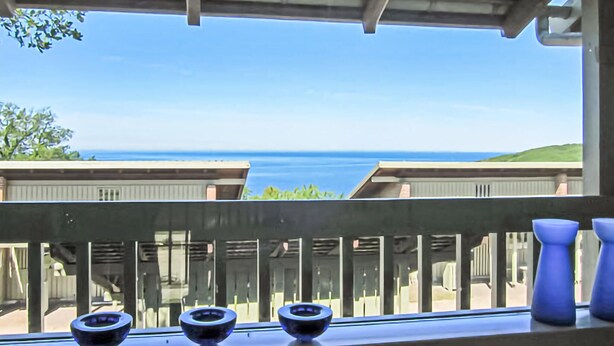 A balcony with a view of the ocean, a railing, and three blue vases.