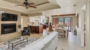 A spacious living room with a fireplace, a ceiling fan, a TV, and a dining area with a wooden table and chairs. - Tucson Escapes at Sabino Ventana King, queen, office, pets, pool, and pickleball (Tucson)