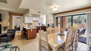 A spacious kitchen with a central island, a dining area with wooden chairs, and a view of the backyard through large sliding glass doors. - Tucson Escapes at Sabino Ventana King, queen, office, pets, pool, and pickleball (Tucson)