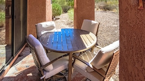 A covered patio with a round table and four chairs, a textured wall, and a view of the desert landscape. - Tucson Escapes at Sabino Ventana King, queen, office, pets, pool, and pickleball (Tucson)