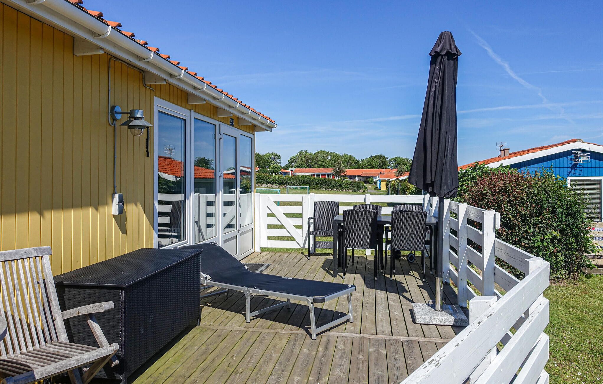 Een houten terras met buitenmeubilair, een overdekte zithoek en uitzicht op de omliggende gebouwen.