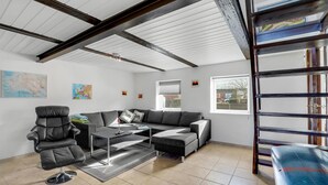 Un salon avec un canapé, une table basse et un fauteuil. Il y a deux fenêtres, une carte accrochée au mur et une échelle.